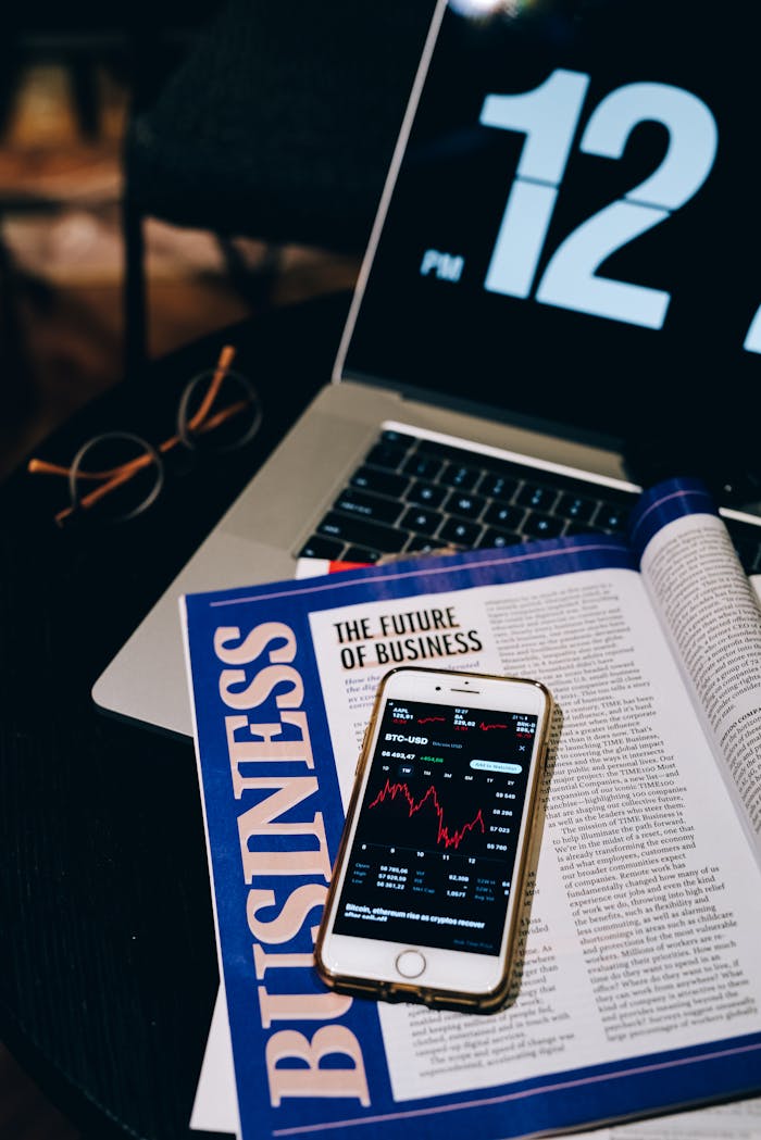 Laptop and smartphone displaying business analytics and cryptocurrency data on a desk with a magazine.